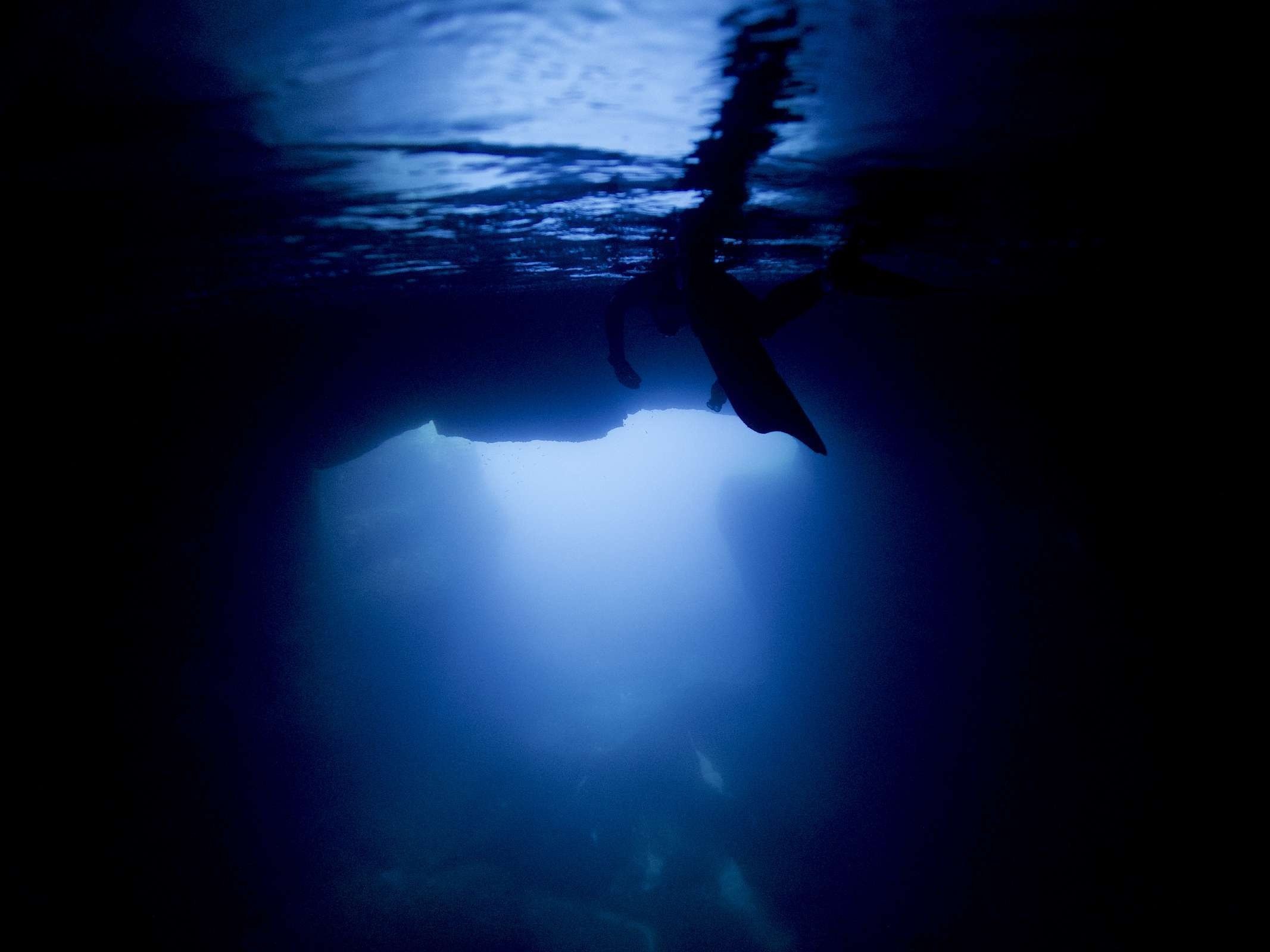 Blick von unter Wasser zur Oberfläche, eine Person schwimmt als dunkle Silhouette gegen das helle Licht.